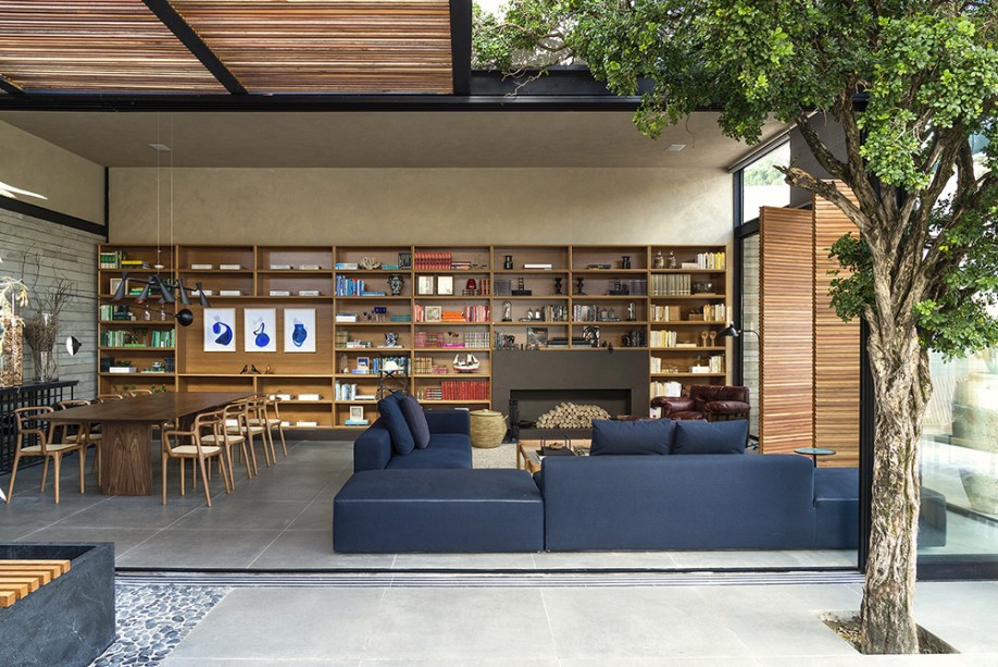 Nando Nunes - Refúgio da Pérgola. A estante na cor louro freijó corresponde à dimensão do espaço, na mesma escala generosa do sofá Herman, dos designers Danilo Lopes e Paula Gontijo. Do lado oposto, vem a mesa de jantar com cadeiras de Andrea Borgoni, lançamento no Salão de Milão. Acima, pendente articulado Zig Zag.