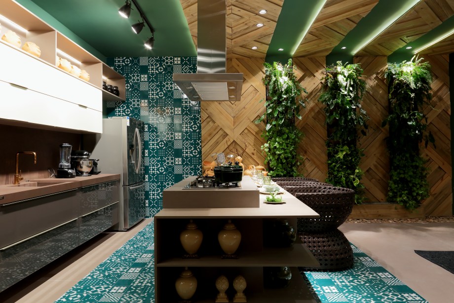 <span>Home Kitchen - Mercia Marinho e Natalia Duarte. O verde dá tom a esse ambiente, que une a funcionalidade de uma cozinha com o aconchego de uma sala de estar. A cor, que está presente nas paredes, nos detalhes da decoração e no exuberante jardim vertical, harmoniza com os tons terrosos e a textura de madeira natural que foi instalada nas paredes e teto em faixas desenhadas com um padrão de losangos de tamanhos diferentes.</span>