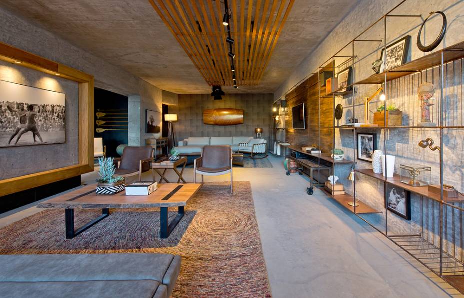 CASACOR Balneário Camboriú. <span>Lounge Al Mare - André Bettinelli e Ana Konradt Lins. Três materiais em estado bruto comandam o ambiente de 98 m²: concreto aparente, madeira e ferro. A estante construída in loco reutiliza ferros e madeira de caixaria da própria obra. O pórtico de madeira, que forma um grande banco, é uma solução para dois pilares desencontrados.</span>