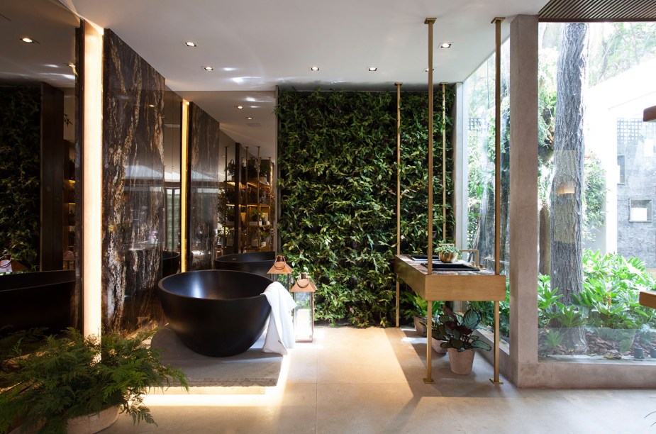 CASACOR São Paulo 2018. <span>SPA da Mata - Andrea Teixeira e Fernanda Negrelli. Com paredes e teto de vidro, a luz natural e o verde fazem parte do ambiente. O contato com as pedras, a madeira e o fogo da lareira, somado aos tons neutros, traz relaxamento. A altura do pé direito é valorizada com elementos verticais, como a fileira de pendentes e as cordas que equilibram as chaises.</span>