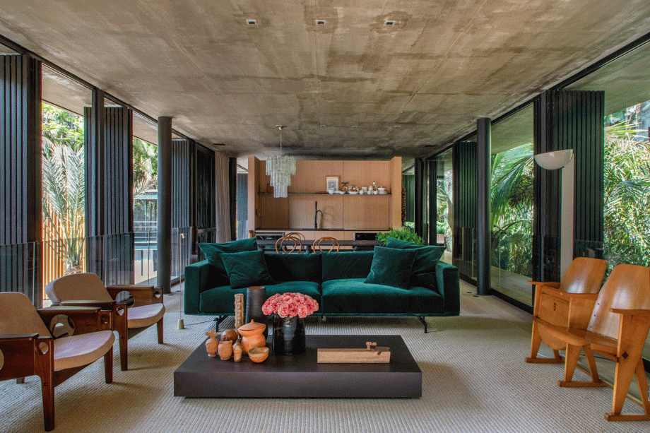 CASACOR Rio de Janeiro. Refúgio Urbano - Bruno Carvalho e Camila Avelar, da BC Arquitetos. As paredes de vidro estabelecem uma relação muito próxima entre a construção e o entorno, com o paisagismo de Daniel Nunes. O layout valoriza a circulação, e os espaços vazios surgem como estratégia para destacar o mobiliário. Entre os protagonistas, o estofado verde e as poltronas em rosa claro, que sobressaem diante da base neutra, com muita madeira, tons de bege e concreto.