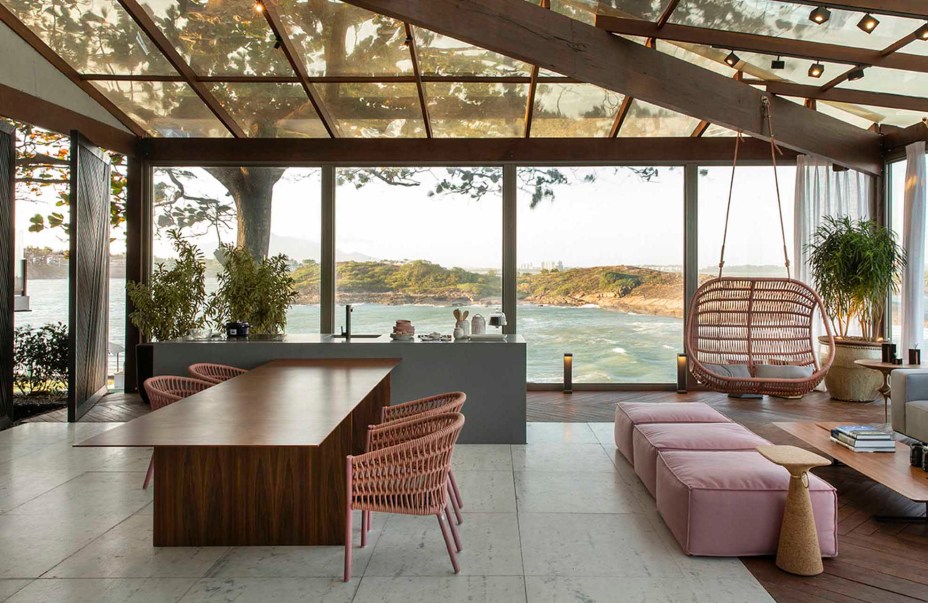 Lounge Sunset - Cyane Zoboli. A arquitetura se integra à paisagem e amplia o alcance da visão, sem perder o conforto de estar em casa. O ambiente de 130 m² emoldura a vista da baía de Vitória e aposta nos recursos naturais, como a madeira e o vidro que conferem simplicidade à estrutura. A ambientação projetada não veio ao acaso, destacando o uso de materiais rochosos, como granito e ardósia, e de madeiras para o deck e mobiliário.