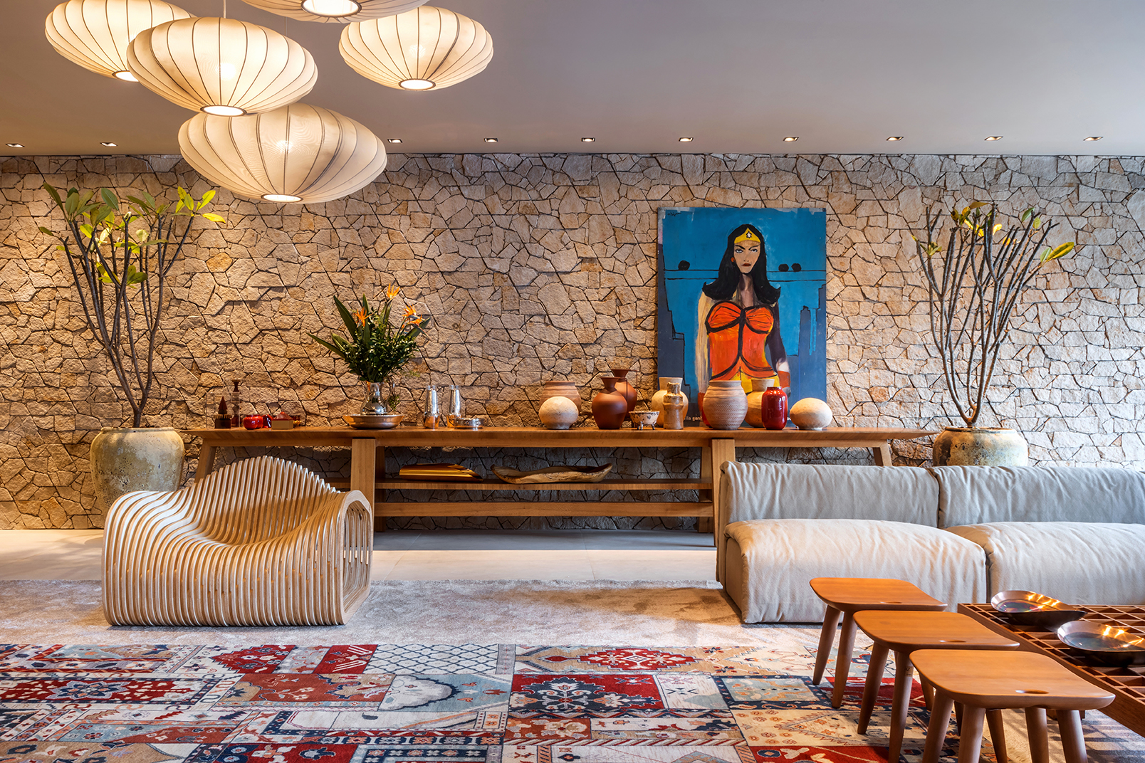 Regina Amaral - Live In. Projeto da CASACOR Goi&aacute;s 2023. Na foto, sala de estar com parede de pedra, quadro e tapete colorido.