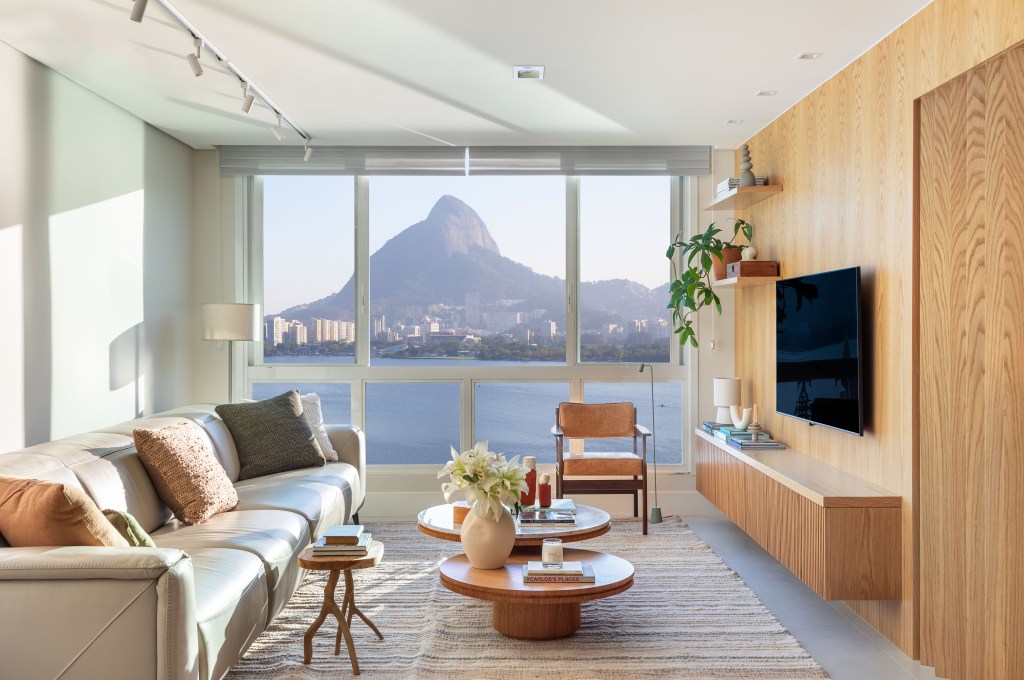 Apartamento de 190 m² tem vista para o Cristo Redentor de todos os cômodos. Projeto Beta Arquitetura. Na foto, sala de estar com tv, parede de madeira e vista para a lagoa.