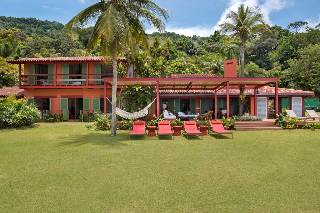 Casa com vista para o mar e nove suítes ganha nova varanda na reforma. Projeto de Escala Arquitetura. Na foto, fachada da casa com jardim e varanda.